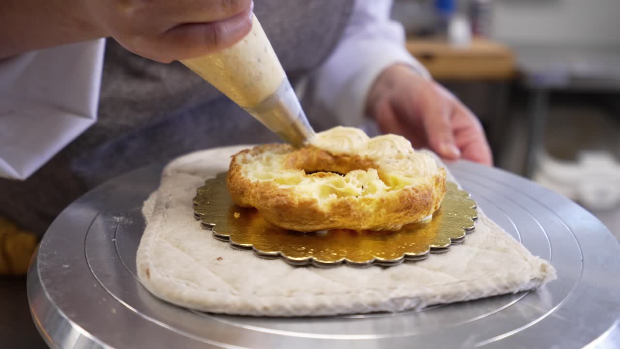 Artisan baker pipes croissant shell with almond cream filling, slow motion close up 4K