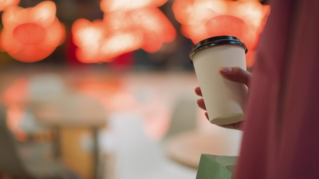 핑크색 드레스를 입고 커피 컵을 들고 레스토랑을 고 있는 여자의 클로즈업, 배경에는 흐릿한 의자, 테이블, 그리고 바닥에 반사되는 밝은 빨간 빛이 있습니다.