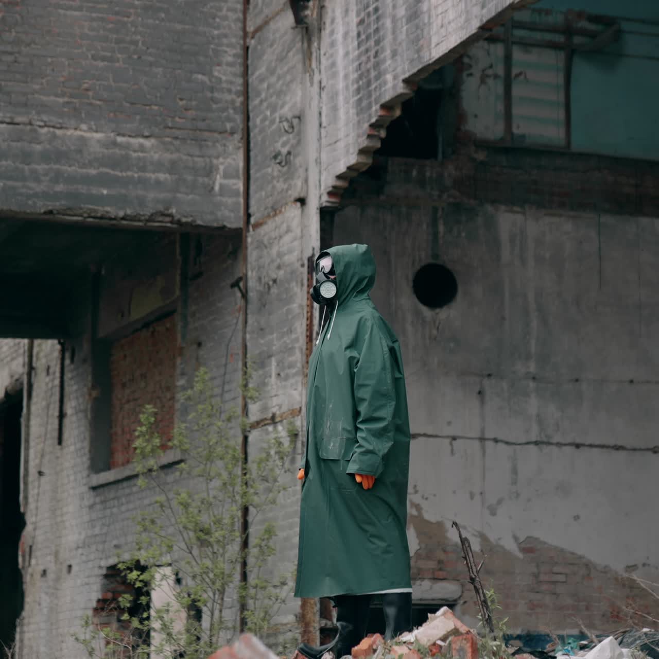 Survivor in abandoned place with radiation. Virologist man in protective costume and respirator gas mask stands in a deserted industrial factory background