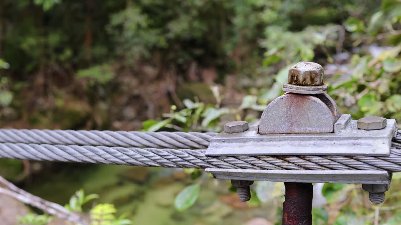 A metal cable with a bolt and nut in a forest environment, showcasing stability and strength