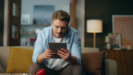 positive man using tab computer at home. optimistic guy working pad sitting sofa