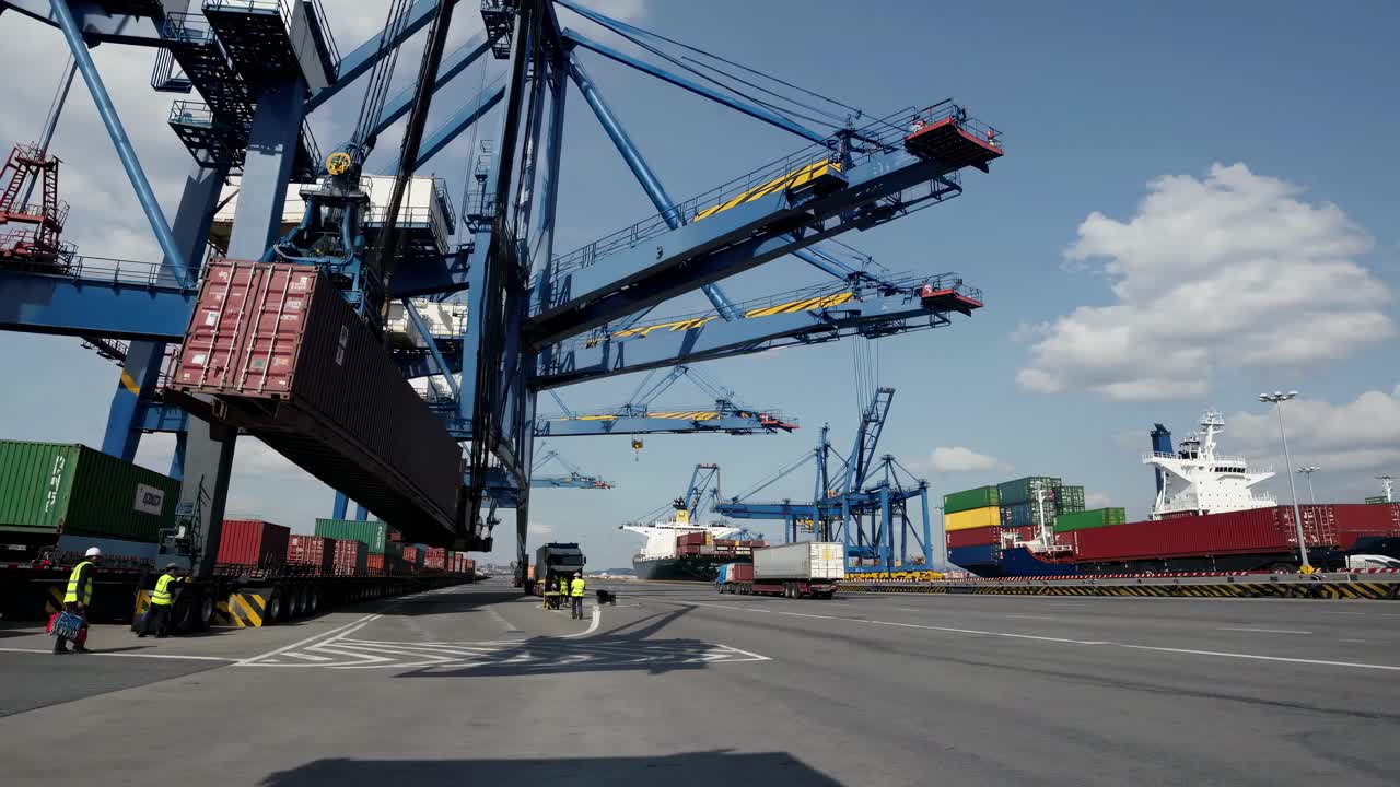 Wide-angle video shot of a bustling port with towering cranes unloading shipping containers