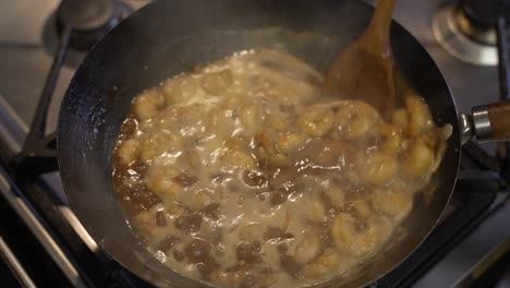 overhead view of prawns being stirred in sauce inside wok with wooden spoon