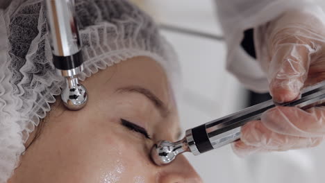 middle-aged woman receiving micro currents facial temples skin treatment from beautician in clinic