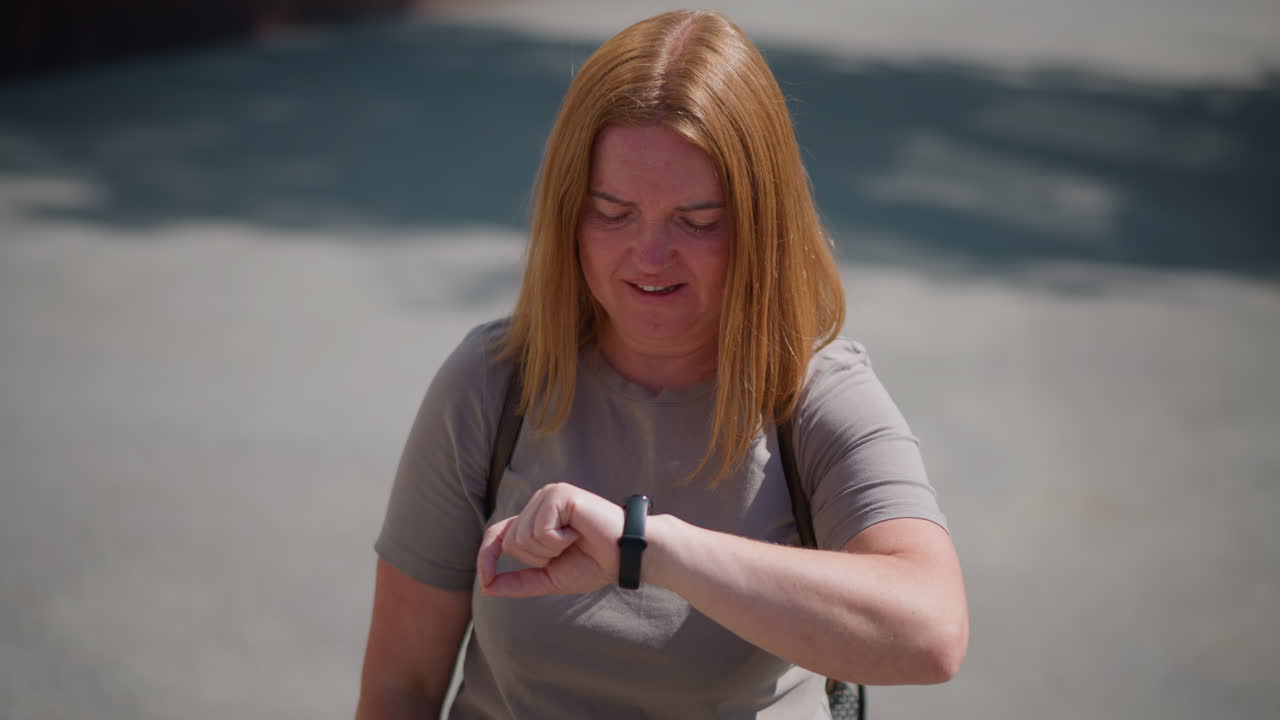 Female student standing outdoors under bright summer sun, checking time on wristwatch with tired expression, sunlight reflecting on face, scene showing heat, fatigue, and anticipation on quiet street