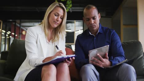 dos colegas de negocios diversos que tienen una charla de video y hacen notas en la oficina