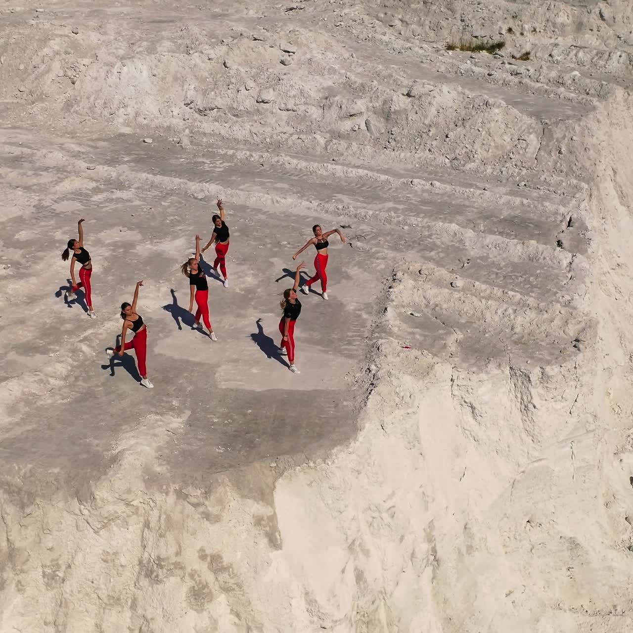 Group of young girls in black tops and red pants dance on the white rock. Active time, hobby outdoors on sunny day. Top view