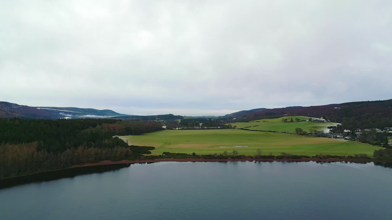 flying parallel to a large grassy meadow on the shoreline of lake Loch Ness