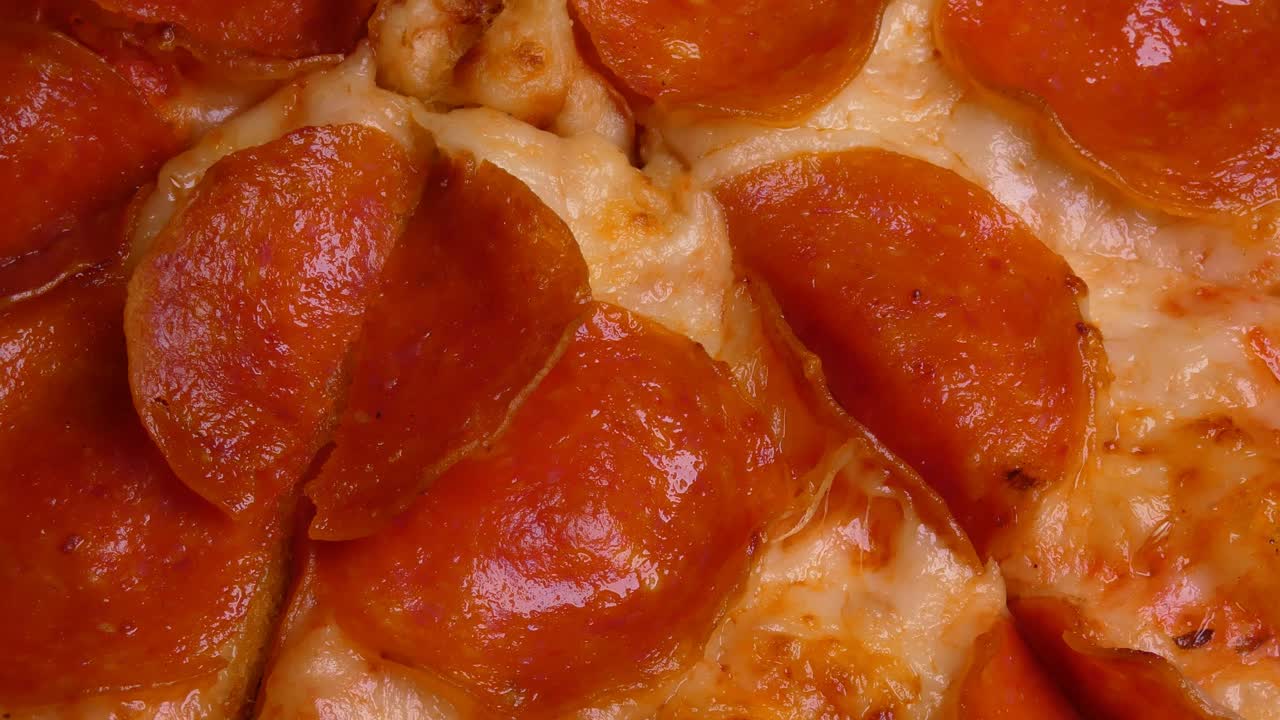 A close up zoomed in shot of a pepperoni cheese pizza. The light above slowly moves around making the shadows move from here to there