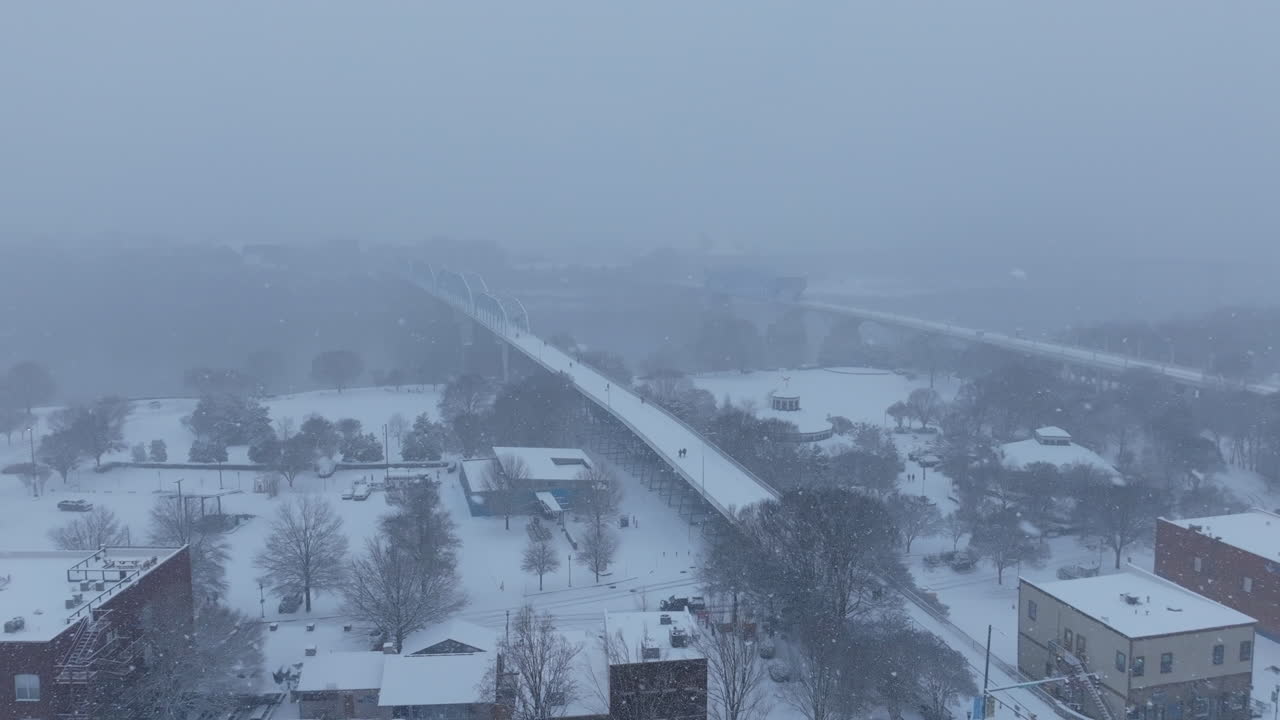 Aerial footage rotating around the Walnut Street Walking Bridge that has people walking on it during a snowstorm in Chattanooga, TN.