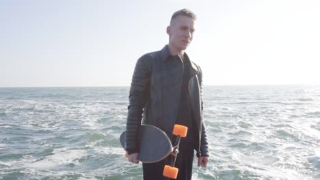 young man holds his longboard standing by the sea