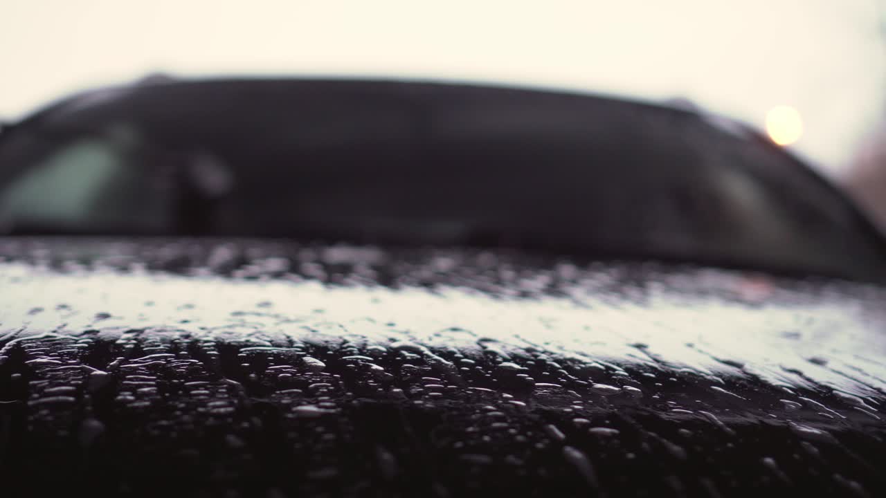 Water, shampoo and foam on car hood, washing front window in background