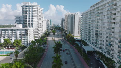 Forwards-fly-above-wide-multilane-road-lined-with-palm-trees-and-tall-buildings-with-white-facades.-Miami,-USA