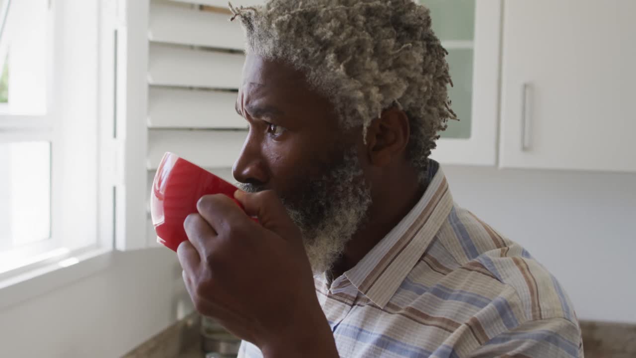 hombre mayor bebiendo café mientras miraba por la ventana en la cocina