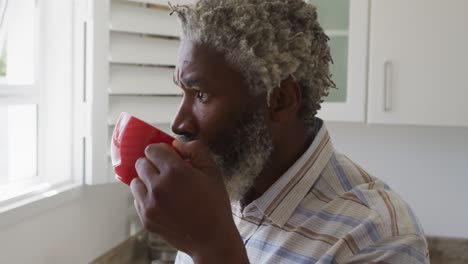 senior man drinking coffee while looking out of window in kitchen