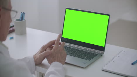 Alter-Arzt-Berät-Online-Laptop-Mit-Grünem-Bildschirm-Auf-Dem-Tisch-Chroma-Key-Konzept