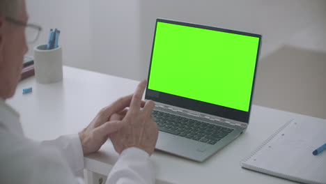 el médico envejecido está consultando en línea portátil con pantalla verde en la mesa concepto de clave croma