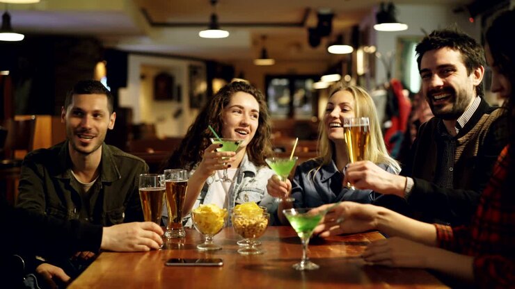 Giovani attraenti si stanno divertendo, bevendo e socializzando insieme in un bar elegante. Gli amici sono felici, si stanno godendo la serata in buona compagnia.