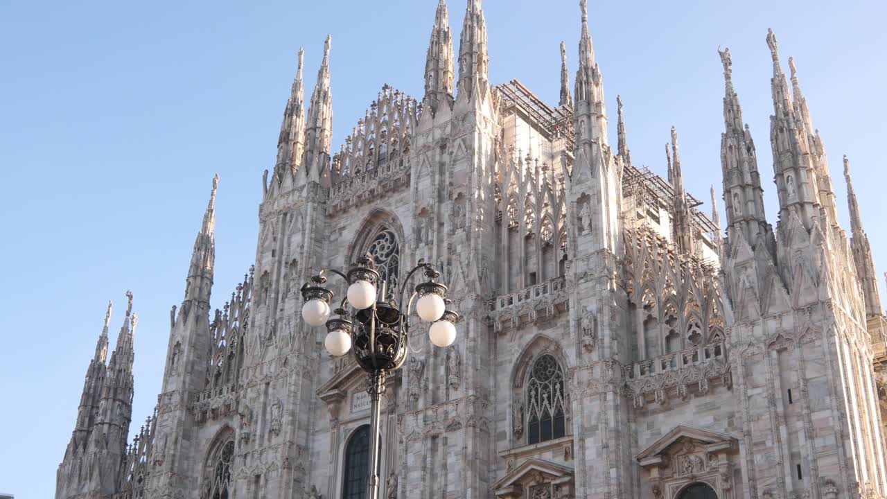 Vista amplia de la magnífica fachada de mármol de la Catedral de Milán con farolas históricas en primer plano