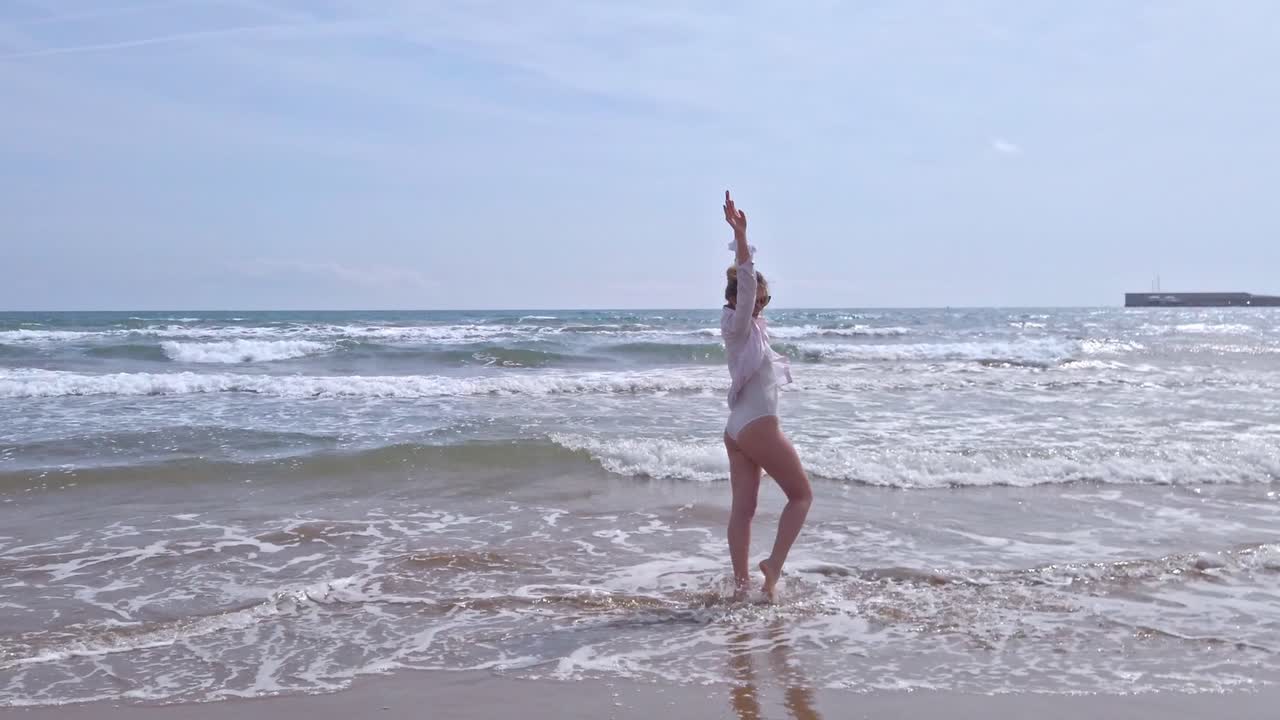 VALENCIA, SPAIN - APRIL 16, 2019: Beautiful young woman dancing happily in the sea. Sea background. Slow motion
