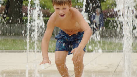 young boy is sitting and running in public water fountain, carefree childhood, slow motion