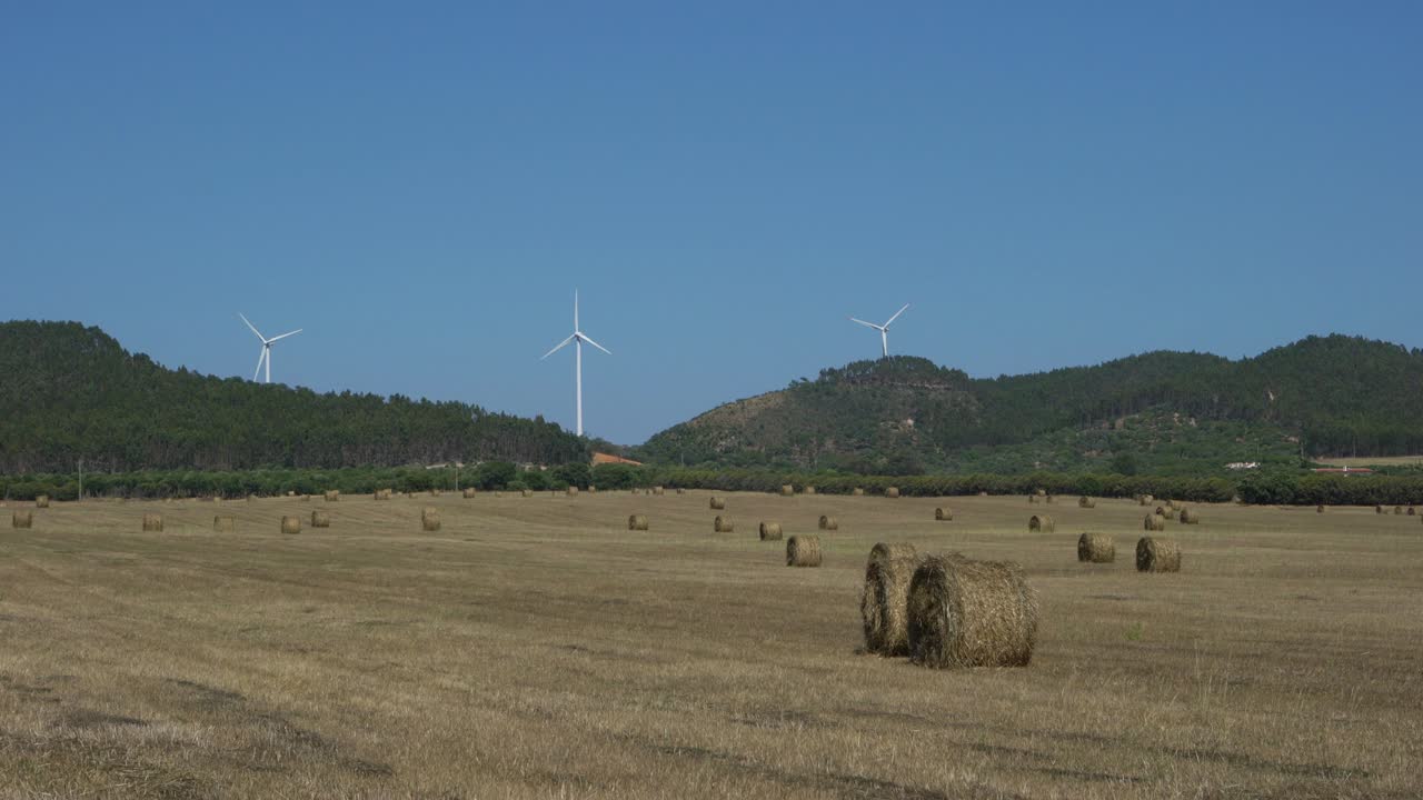 campo con rollos de heno esparcidos con una granja eólica en el fondo