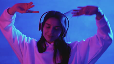 mujer joven feliz bailando y escuchando música con auriculares inalámbricos en un colorido fondo de luz de neón