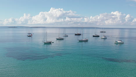 Boats-On-The-Turquoise-Waters-Of-Playa-de-ses-Salines-In-Ibiza,-Spain---aerial-pullback