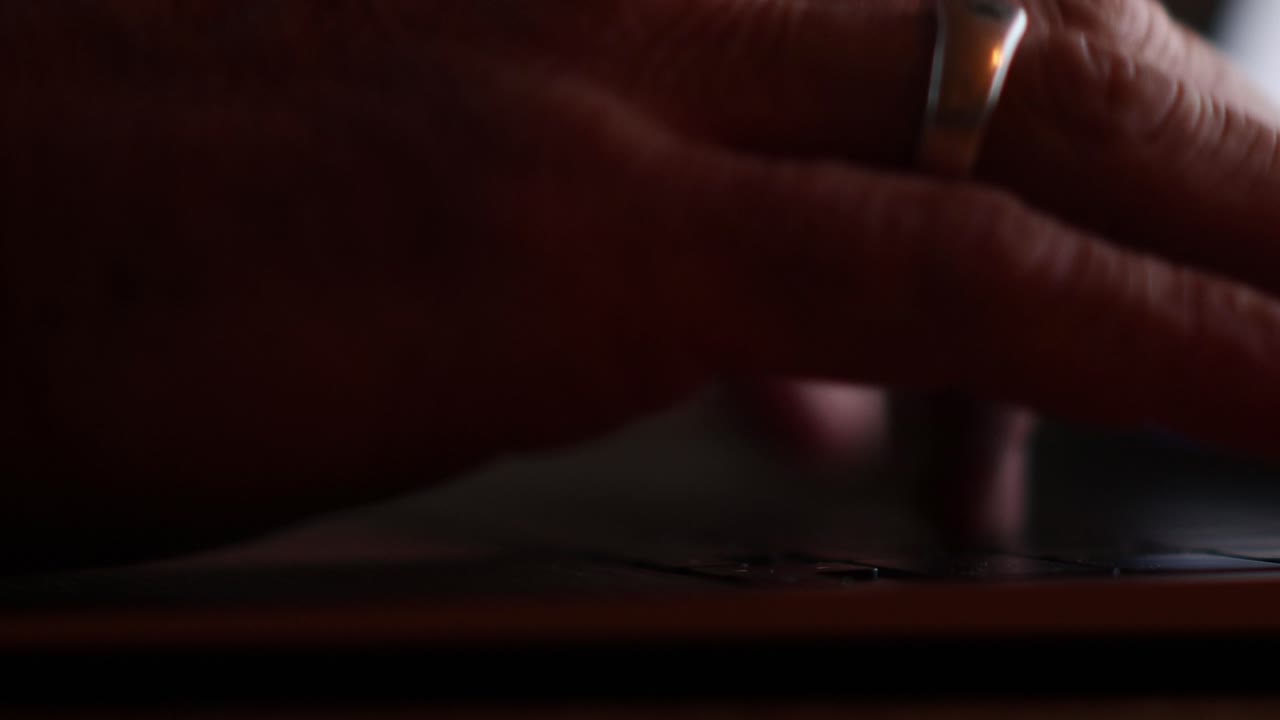 närbild av en mans händer som skriver på en bärbar dator lätt upplyst av skärmen