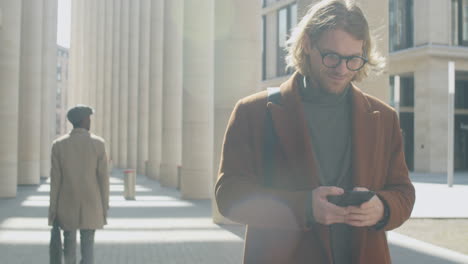 businessman walking outdoors and messaging on smartphone