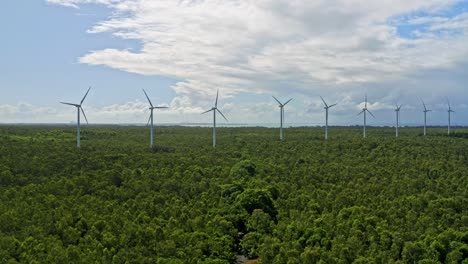 spinning wind turbines against blue sky in lush forested onshore area