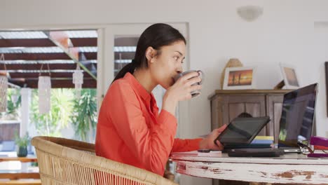 mujer biracial usando una computadora portátil y trabajando en la sala de estar