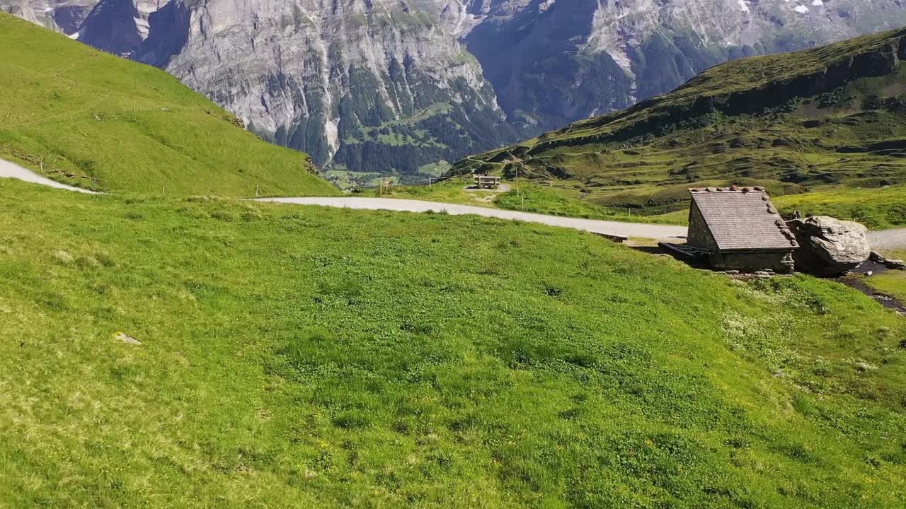 disparo aéreo de un excursionista que camina junto a una pequeña cabaña de madera en una ruta de senderismo con vistas a las montañas de los alpes suizos cubiertas de nieve schreckhorn y finsteraarhorn en verano