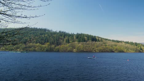 Man-fishing-on-a-boat-casting-fishing-pole-in-Lady-Bower-Reservoir-sunny-day-waves-moving-calm-sailing-in-the-peak-district-shot-in-4K