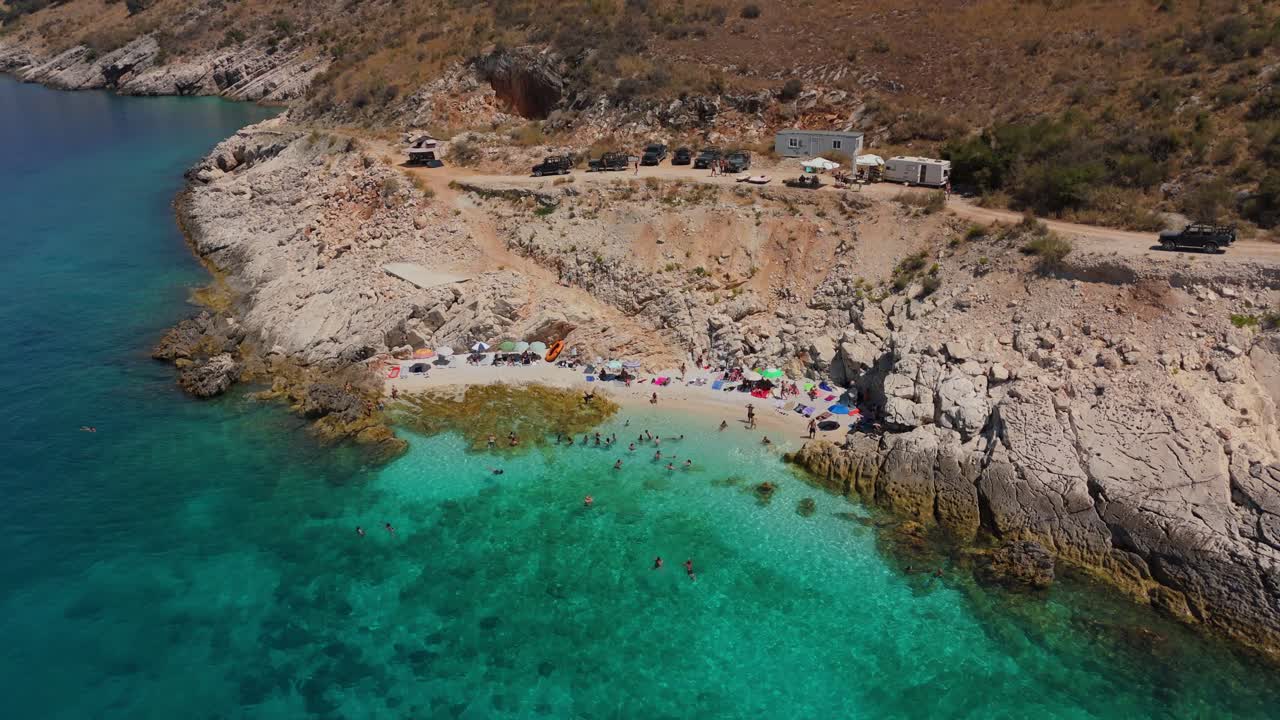Remote Albanian beach with crystal-clear water, few visitors, and rocky surroundings