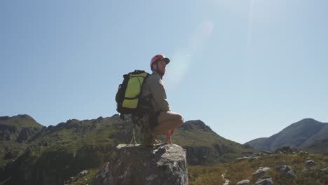 young caucasian man crouching on a rock