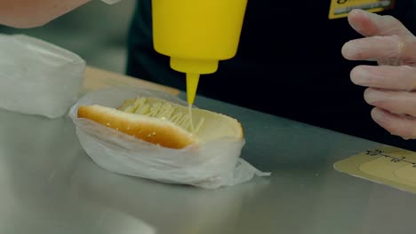 cu cocinero en cámara lenta prepara un perrito caliente vierte mostaza en el pan