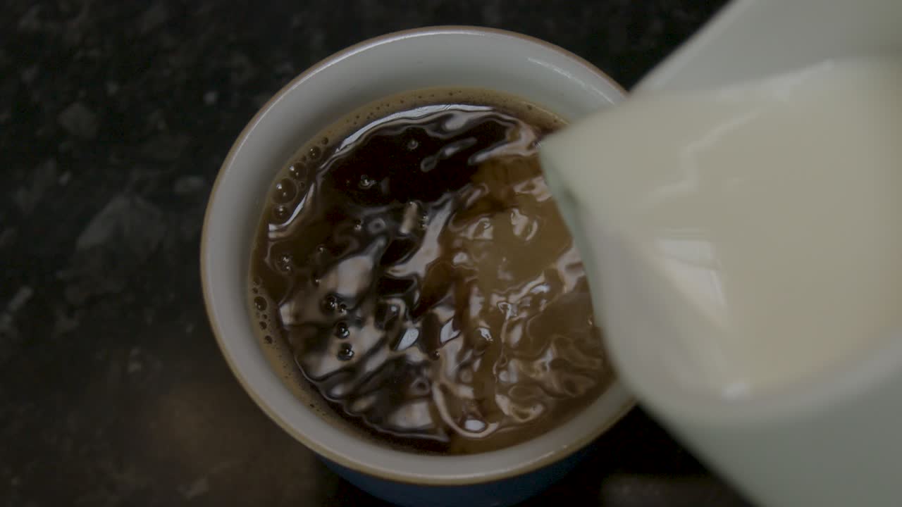 Pouring milk into a mug of black instant coffee in slow motion