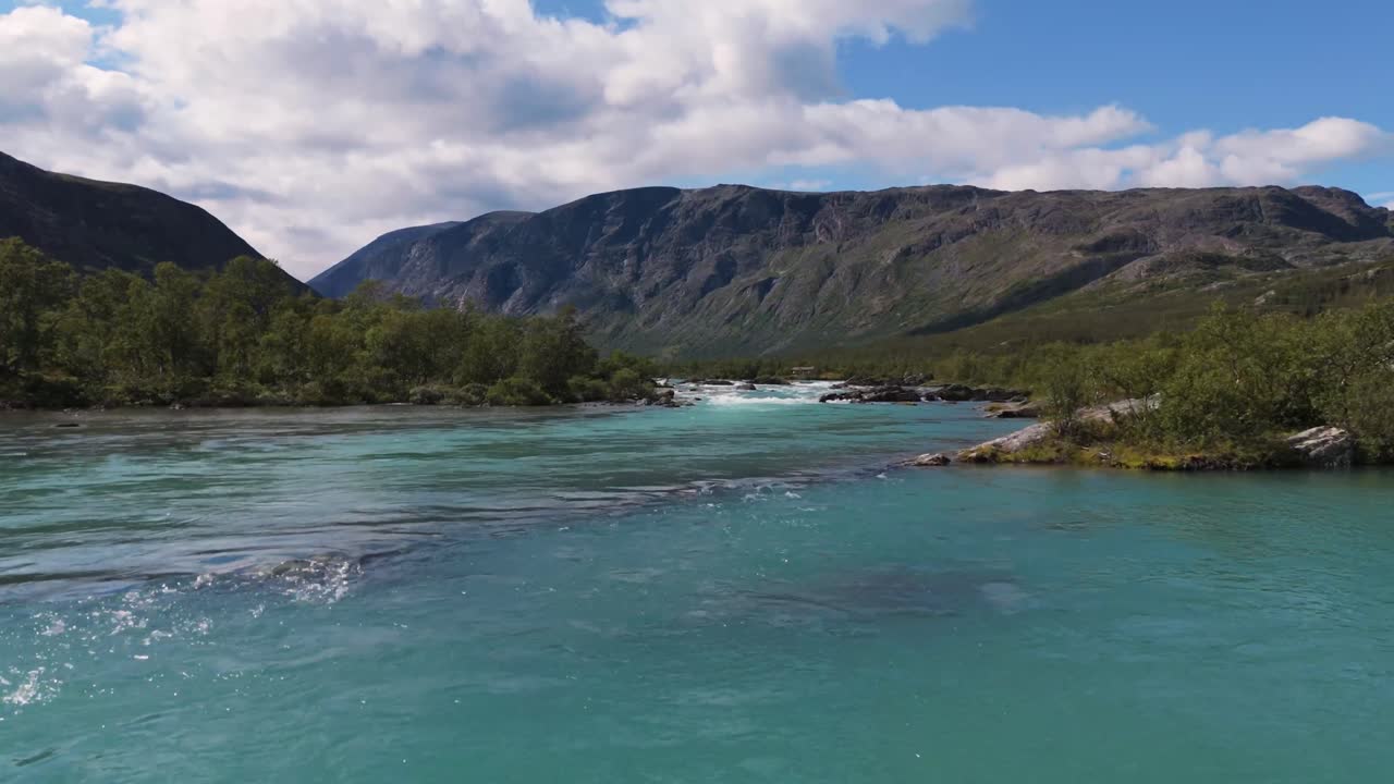 Aerial low flying over turquoise river flowing between lush green mountains. Captures the beauty of nature and serene landscapes.