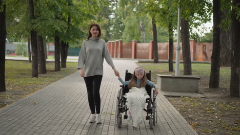 little girl sits in wheelchair holding hand of caring mother