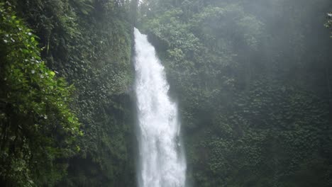 Slow-motion-panning-up-shot-in-front-of-a-gushing-NungNung-Waterfall-in-Bali,-Indonesia-following-a-rain-storm