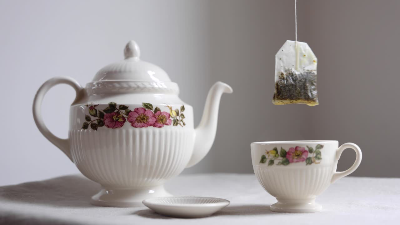 Einen Teebeutel aus einer Teetasse mit Blumenmuster neben einer Teekanne heben