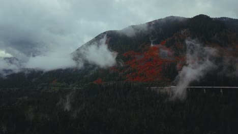 washington state - drone aerial static of a misty pine forest and mountains with a highway, trucks, and cars, and red fall colours near franklin falls and snowqualmie