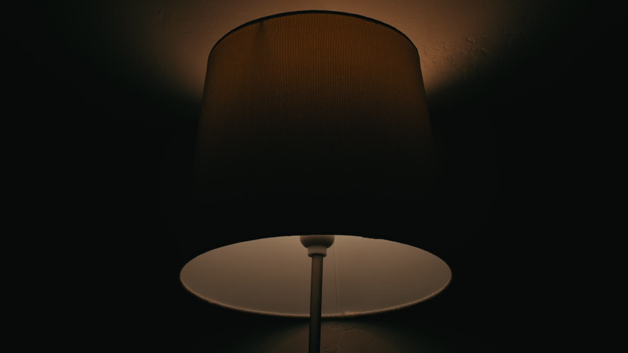 Inquadratura dal basso verso l'alto di una lampada tremolante che proietta ombre in una stanza buia, penne in una tazza