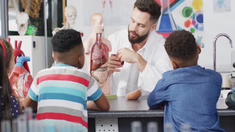 Vielfältiger-Männlicher-Lehrer-Und-Glückliche-Schulkinder,-Die-Im-Biologieunterricht-Das-Modell-Des-Menschlichen-Körpers-Studieren