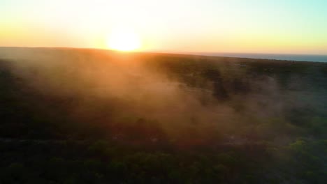 misty haze fog smoke rises spread across shrub landscape at golden hour orange glow in air