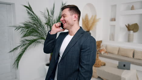 resilient caucasian man speaking on the phone. man in jacket stands in the room laughing cheerfully during phone conversation.