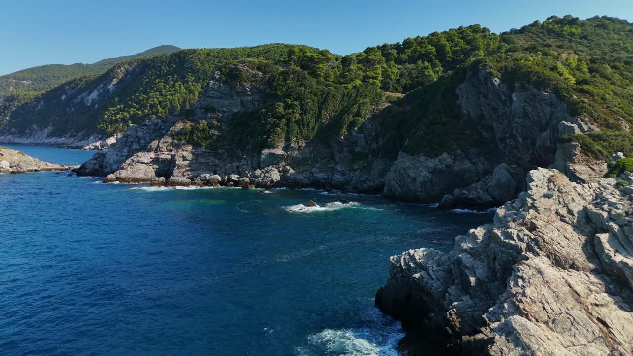 Costa rocciosa con rigogliose colline verdi e mare blu profondo sotto un cielo sereno, vista aerea.