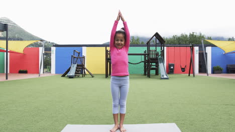 in a school playground, a young african american girl practices yoga