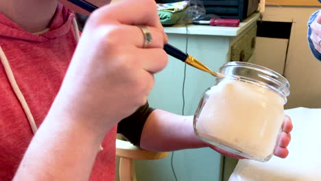 Teenage-boy-smiling-while-painting-mason-jars-with-white-paint-for-turning-them-into-vases-at-an-upcoming-event